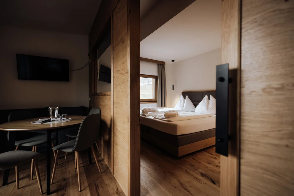 Hotelzimmer mit Doppelbett und kleinem Essbereich, getrennt durch eine Holzschiebetür