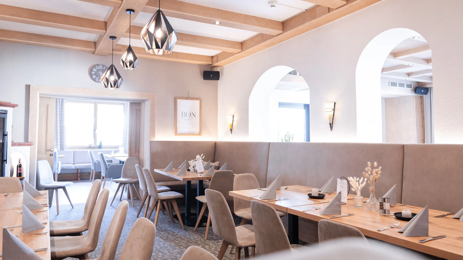 Heller Restaurantbereich mit gedeckten Tischen, gepolsterten Stühlen und Pendelleuchten