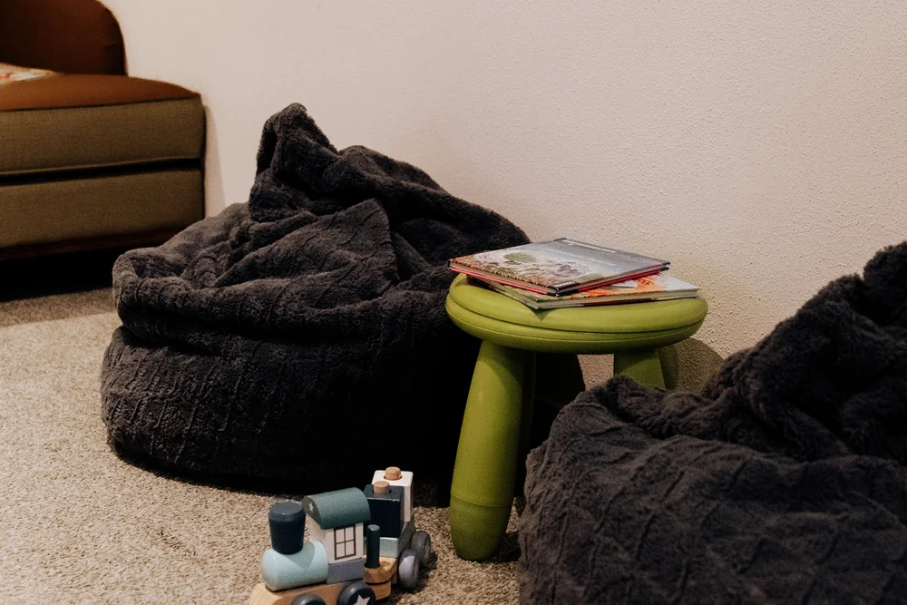 Zwei dunkle Sitzsäcke, ein grüner Hocker mit Büchern und eine Spielzeugeisenbahn auf Teppichboden