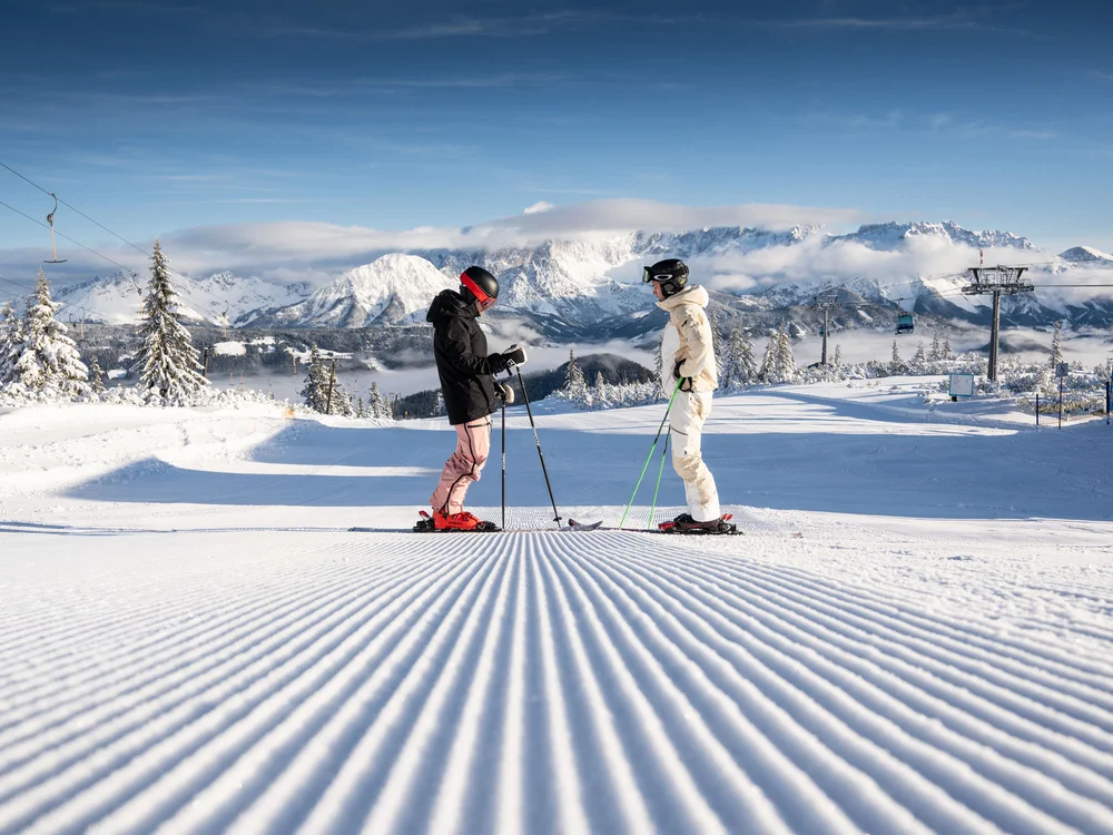 Winterurlaub beim Forstauerwirt Zwei Skifahrer auf einer präparierten Piste vor einer verschneiten Bergkulisse