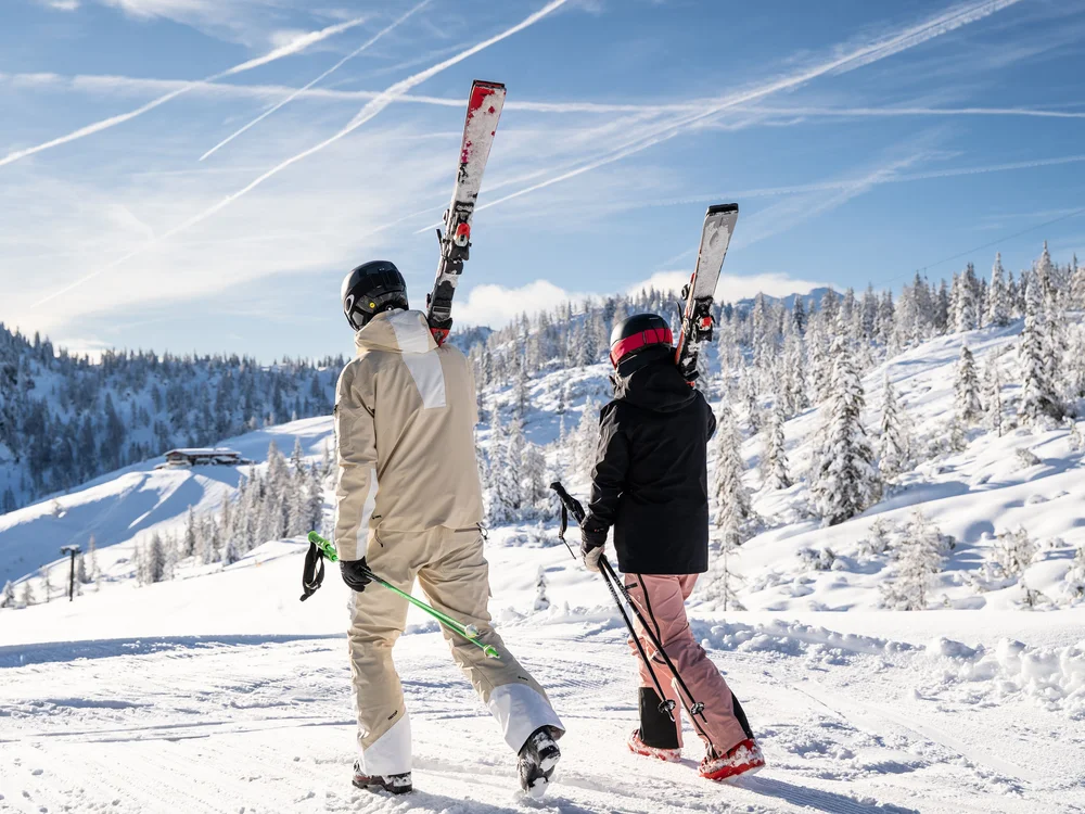 Winterurlaub beim Forstauerwirt Zwei Skifahrer tragen ihre Ski und Stöcke durch eine verschneite Berglandschaft