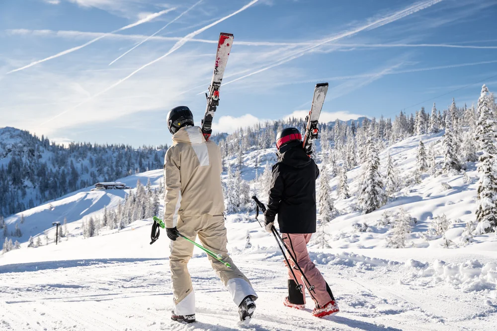 Zwei Skifahrer tragen ihre Ski und Stöcke durch eine verschneite Berglandschaft