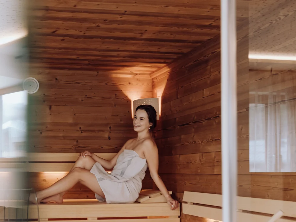 Winterurlaub beim Forstauerwirt Frau im Handtuch sitzt auf einer Holzbank in der Sauna