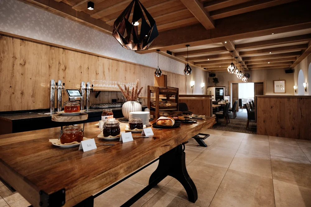Frühstücksbuffet mit Marmelade, Brot und Geschirr auf einem Holztisch im gemütlichen Speisesaal