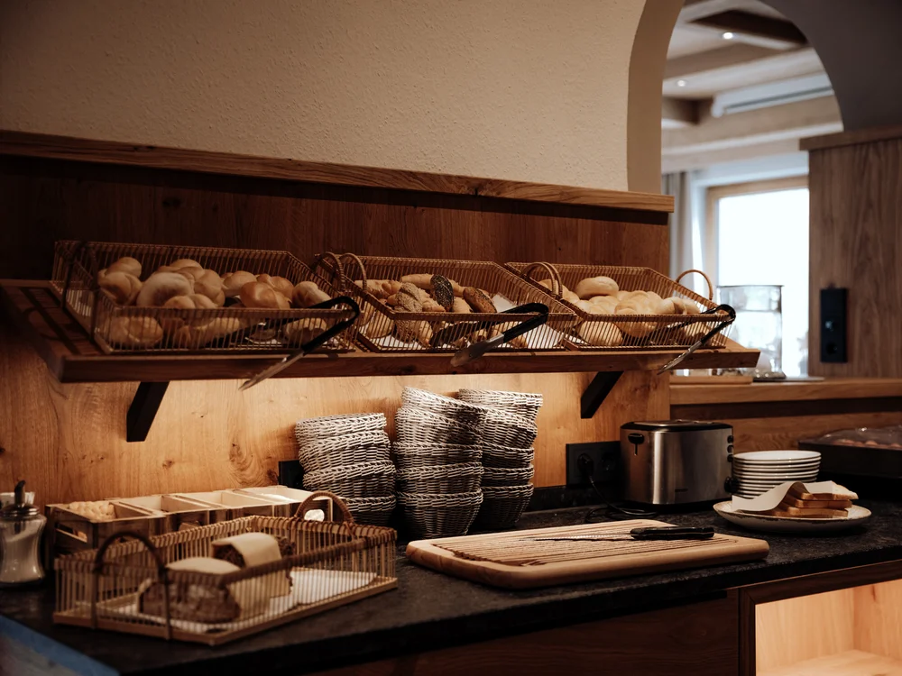 Winterurlaub beim Forstauerwirt Frühstücksbuffet mit Brotkörben, Körben und einem Toaster auf einer Holztheke