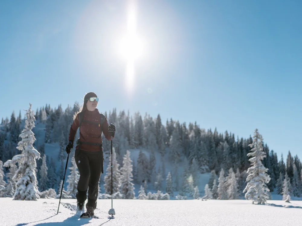 Winterurlaub beim Forstauerwirt Frau mit Skistöcken auf einer sonnigen, verschneiten Loipe