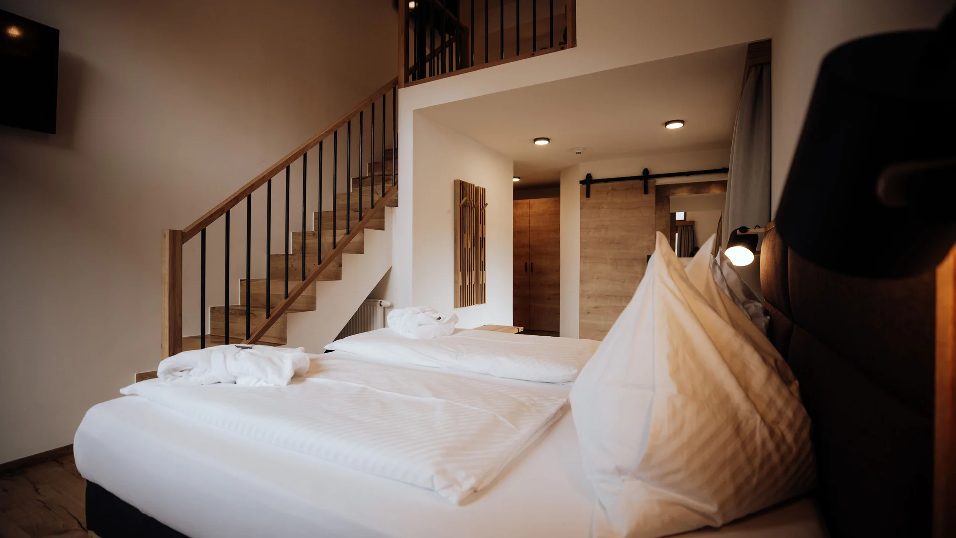 Hotelzimmer mit zwei weißen Betten und einer Treppe zur Galerie