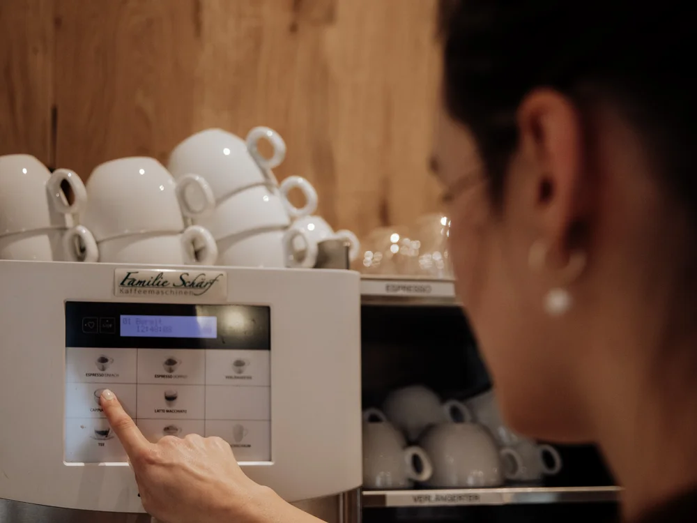 Winterurlaub beim Forstauerwirt Frau wählt an einem Kaffeeautomaten ein Getränk; Tassen stehen im Regal