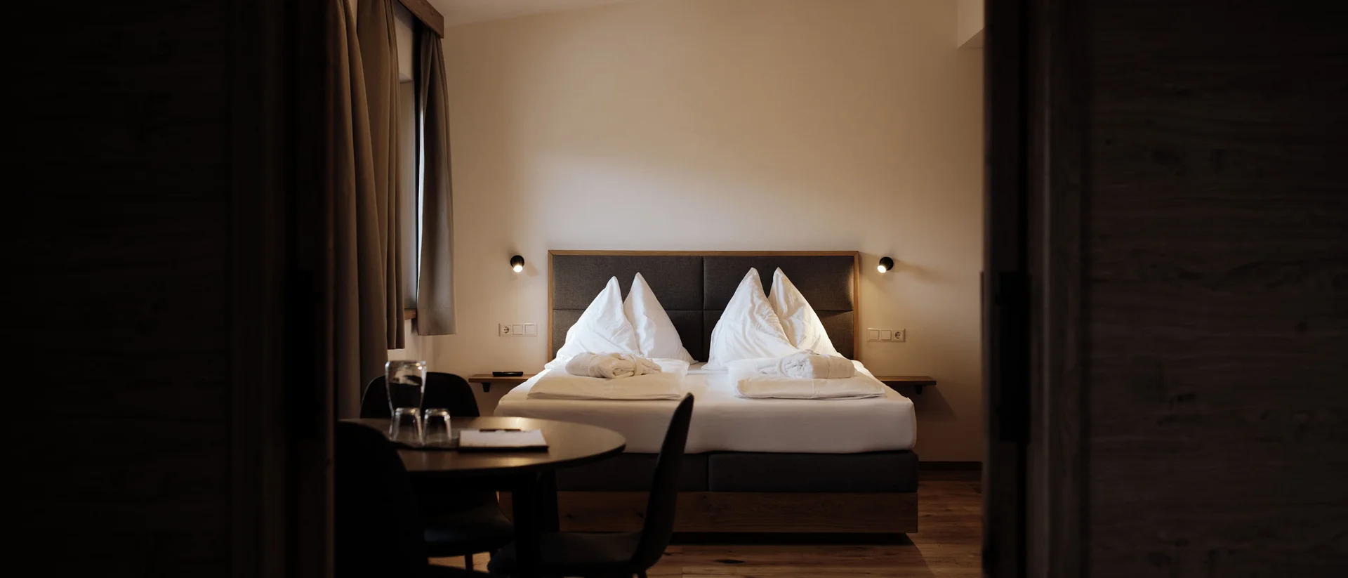 Winterurlaub beim Forstauerwirt Hotelzimmer mit großem Bett, weißer Bettwäsche und Tisch mit Stühlen