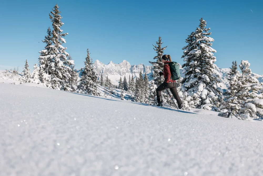 Wanderin mit Rucksack und Stöcken in einer verschneiten Berglandschaft
