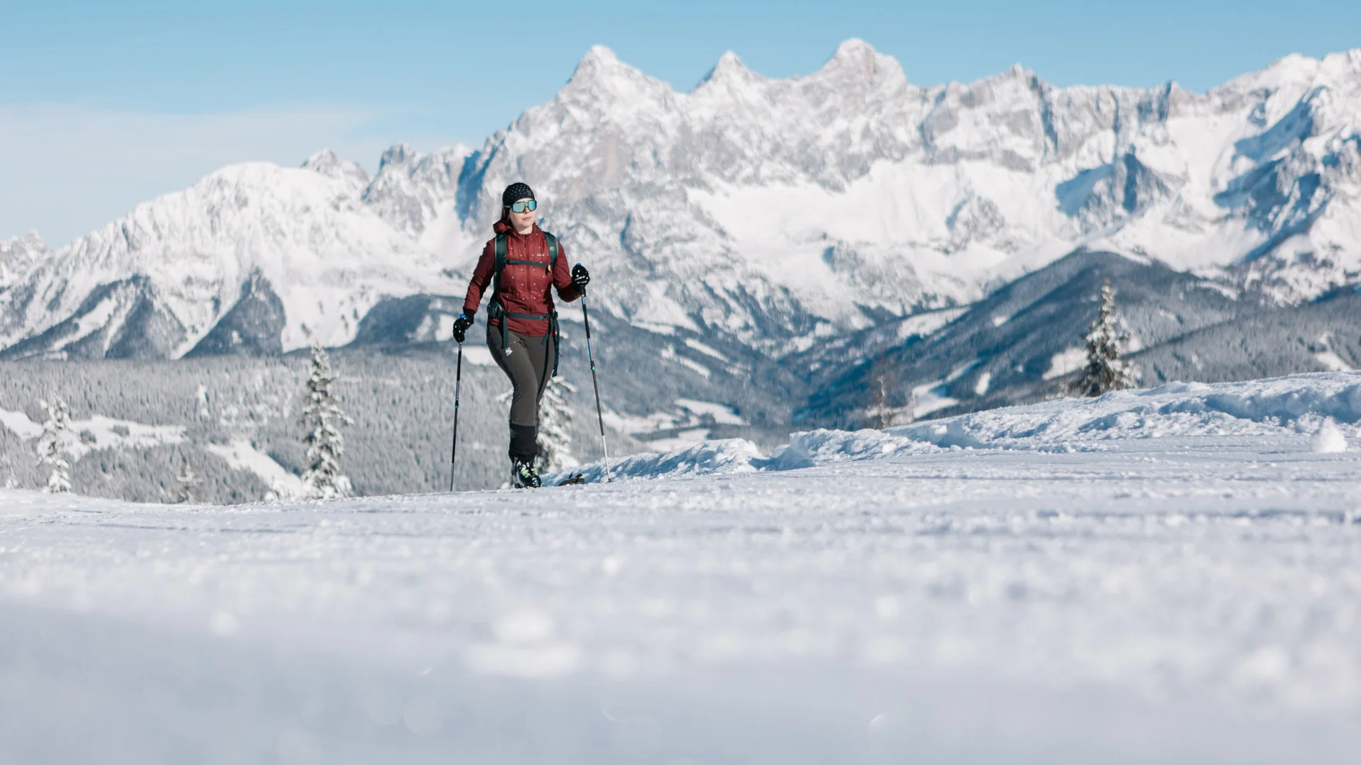 Skifahrerin mit Stöcken auf einer verschneiten Loipe vor schneebedeckten Bergen