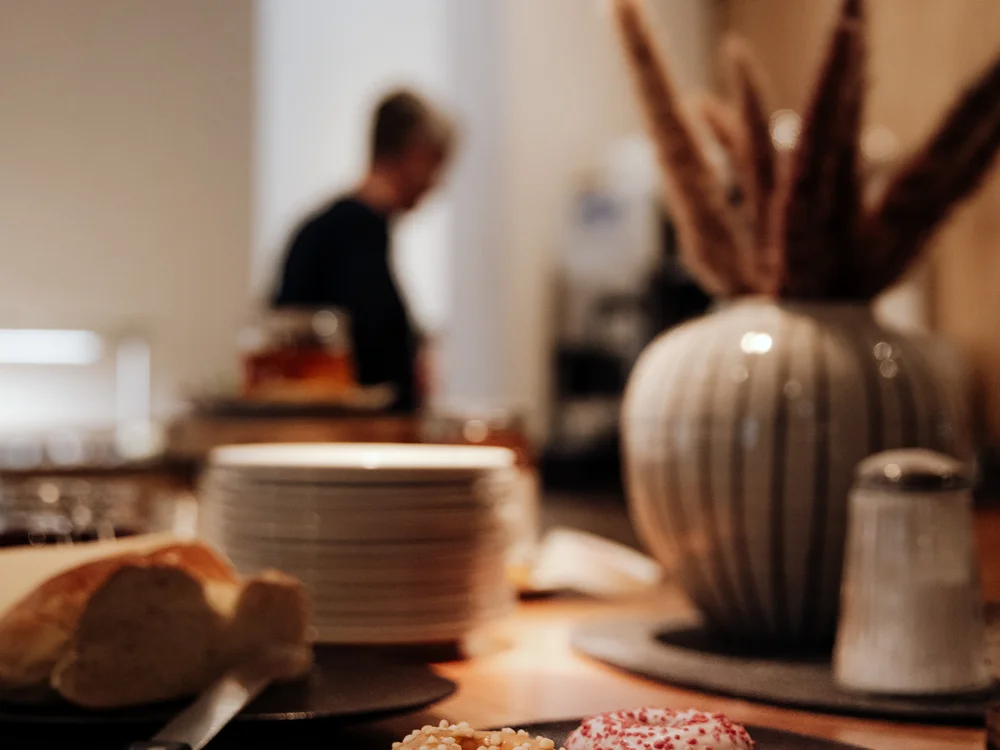 Winterurlaub beim Forstauerwirt Vier verzierte Donuts auf einem Teller, dahinter ein unscharfer Mitarbeiter