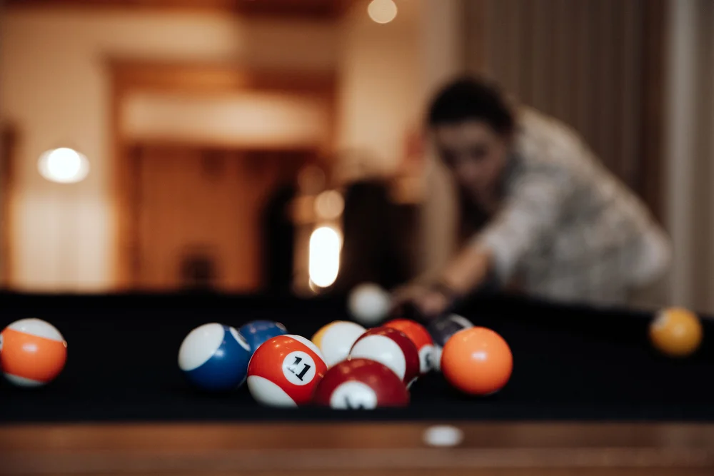 Billardkugeln auf dem Tisch, während eine Person im Hintergrund spielt