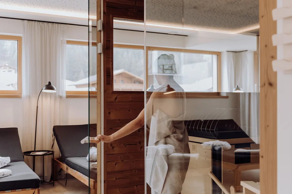 Frau öffnet eine Glastür in einem Wellnessbereich mit Liegen
