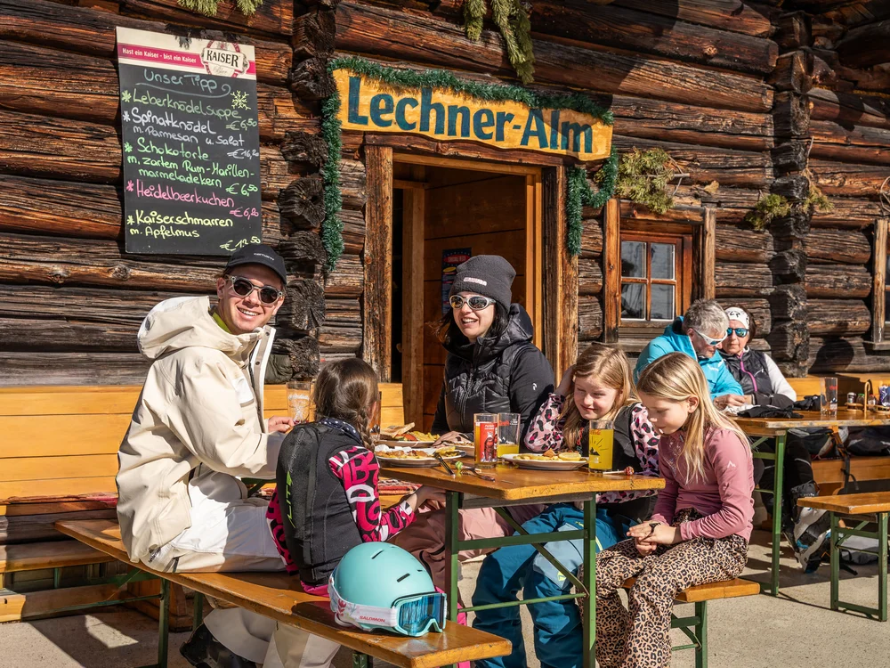 Winterurlaub beim Forstauerwirt Familie beim Essen vor der Lechner-Alm, einer rustikalen Holzhütte