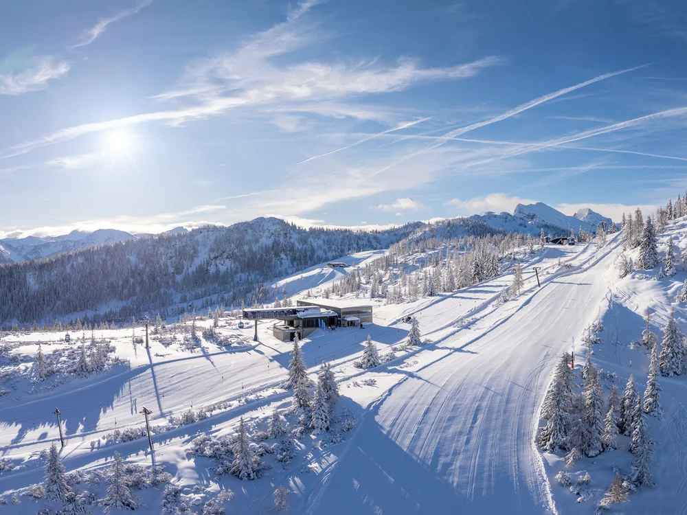 Winterurlaub beim Forstauerwirt Verschneite Skipisten und Liftanlagen vor bewaldeten Bergen unter blauem Himmel