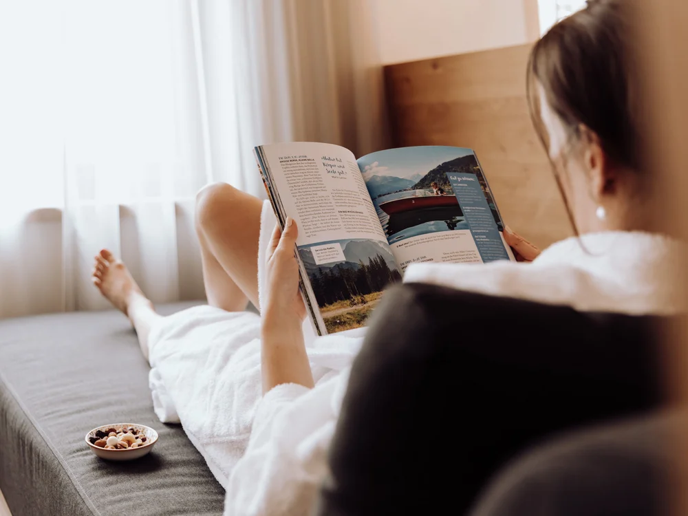 Winterurlaub beim Forstauerwirt Frau entspannt im Bett und liest eine Zeitschrift, daneben steht eine Schale mit Snacks