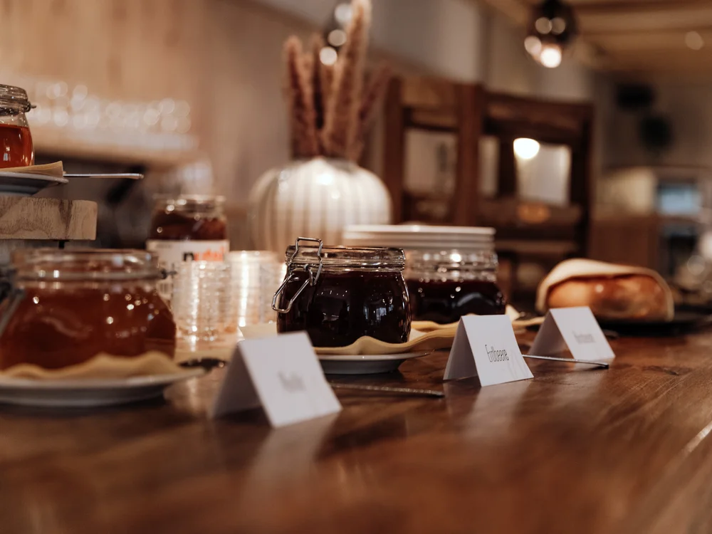 Winterurlaub beim Forstauerwirt Gläser mit Marmelade auf einem Frühstücksbuffet aus Holz, dahinter ein Brötchen